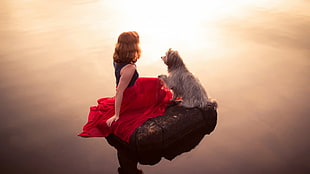 woman in black and red dress sitting beside long-coated gray dog on rock in middle of water HD wallpaper