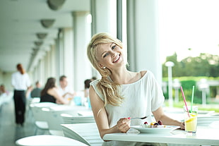 selective focus photography of woman in white blouse holding spoon while slightly tilting her head while smiling