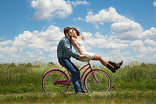 man on blue checkered flannel kissing by a girl wearing white spaghetti strap dress riding on red bicycle during day time HD wallpaper