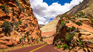 landscape photo of black top road near brown rock formation under cloudy sky during daytime