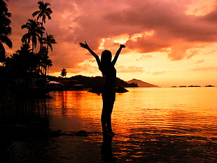 silhouette ow woman standing on water during sunset