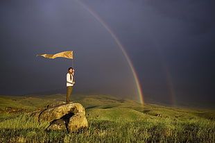 man holding flag standing on rock near grass field HD wallpaper
