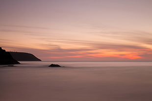 calm body of water beside silhouette of mountain during golden hour photo