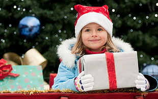 girl in blue jacket with red santa hat holding gift box HD wallpaper