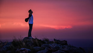 man wearing white crew neck shirt standing on gray rock during dawn HD wallpaper