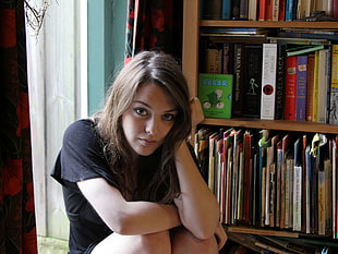 woman wearing black t-shirt sitting near brown wooden book shelf at daytime HD wallpaper
