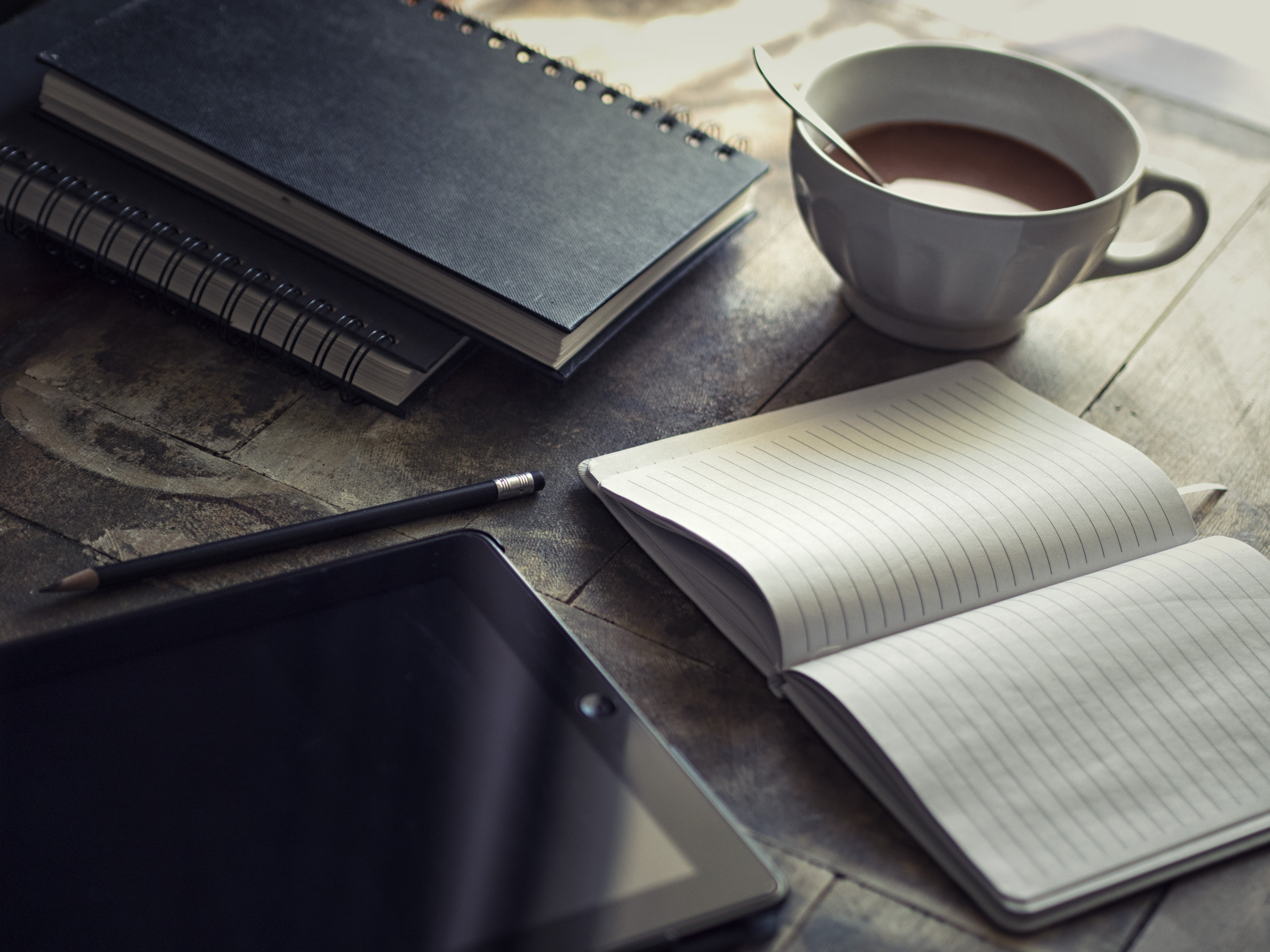 black iPad beside pen and open notebook on gray ceramic tile surface