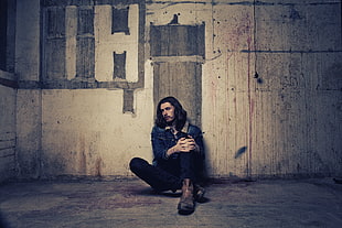 man in blue denim jacket sitting beside gray concrete wall HD wallpaper