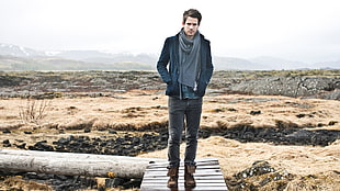 man wearing coat and pants walking on bridge looking on camera