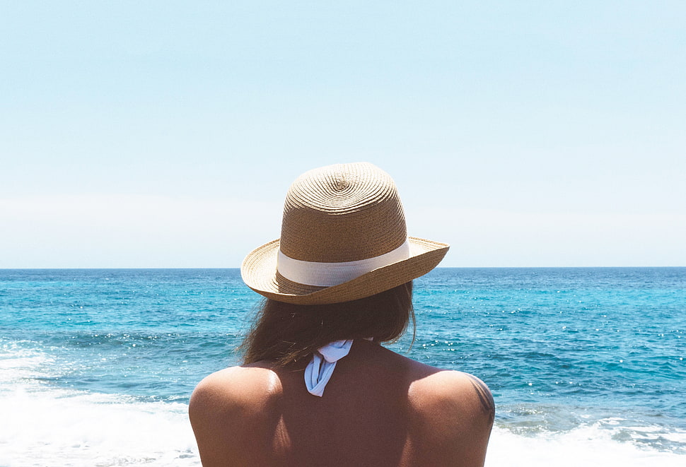 woman with brown bucket hat standing on seashore during daytime HD wallpaper