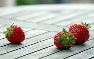 macro photography of three strawberries on gray wooden surface