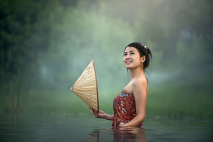 woman in red floral tube top holding brown hat