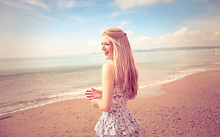 blonde haired woman in purple and white floral dress in front of beach while laughing HD wallpaper