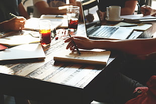 person holding black pen on brown notebook