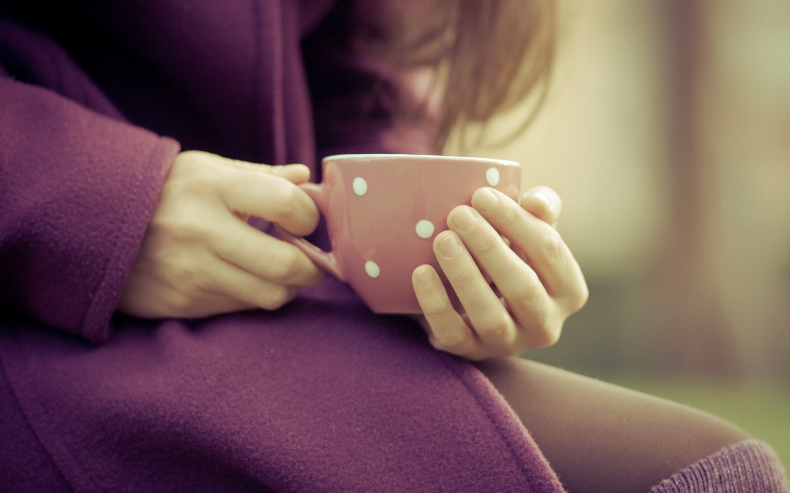 person wearing purple long-sleeve top holding white and pink polka-dotted tea cup