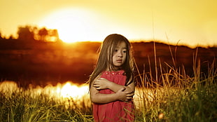 girl in red dress surrounded by green grass during yellow sunset HD wallpaper