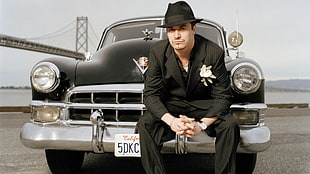 man in black suit sitting on classic black car over looking suspension bridge HD wallpaper