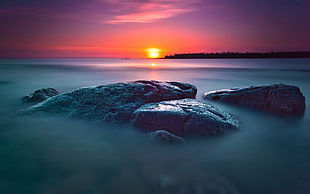 gray rock formation near body of water at sunset