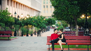 man and woman sitting on red bench talking to each other HD wallpaper
