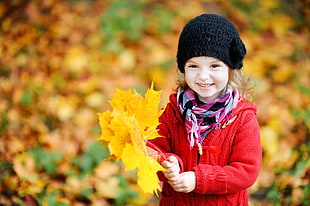 girl wearing red jacket and black beanie holding brown maple leaf HD wallpaper