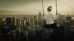 macro photography of girl sitting on swing with high rise building background HD wallpaper
