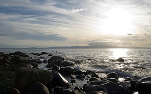 rocks near the body of water under white clouds during daytime