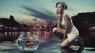 woman in white body con dress looking at glass bowl with gold fish HD wallpaper