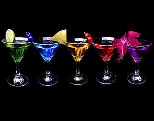 five cocktail glasses filled with assorted liquids