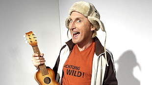 man wearing white and black zip-up top holding ukulele in the white wall paint room