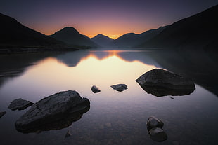 gray rocks on body of water surrounded by mountains