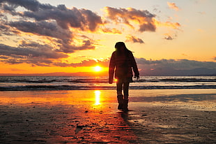 person wearing coat standing on sea side facing the sun at sea