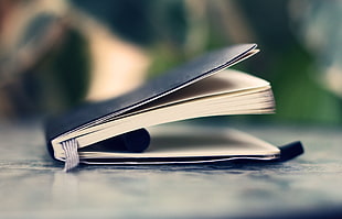 focus photo of black labeled book with bookmark and pen