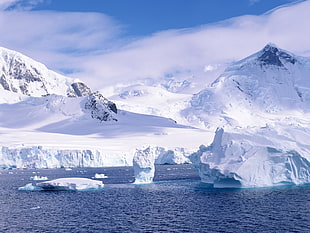 body of water near mountain peaks under blue sky