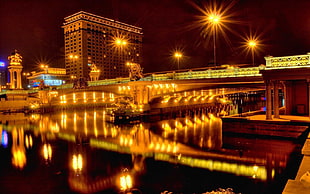 photography of lightened beige bridge over water near building