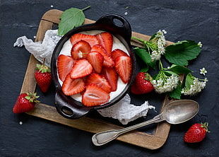 black cooking pot of strawberries with milk beside silver ladle
