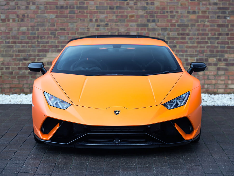 orange Lamborghini Huracan parked near brown brick wall HD wallpaper