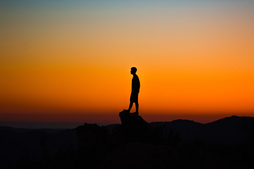 silhouette of man on top of rock formation HD wallpaper