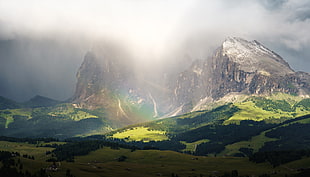 snowy mountain behind the green field grass and trees with fog and rainbow