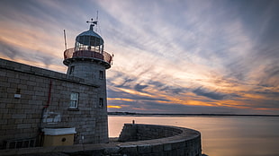 gray concrete light tower beside body of water during sunset, howth, dublin, ireland