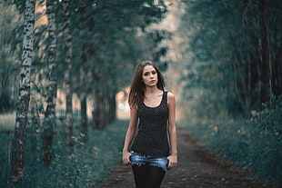 woman in black and white tank top standing surrounded by trees