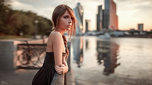woman in black and grey dress standing near calm body of water and concrete buildings during daytime HD wallpaper