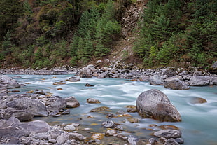 photography of rocks on river beside mountain slope HD wallpaper