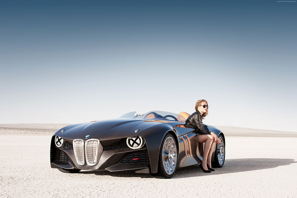 female sitting on black sports convertible on desert HD wallpaper