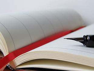 fountain pen on white book with red ribbon bookmark