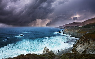 sea waves hitting near stone cliff under gray cloudy sky during daytime HD wallpaper