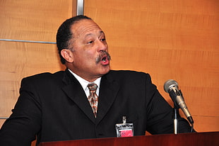 man wearing formal suit speaking in front of microphone HD wallpaper
