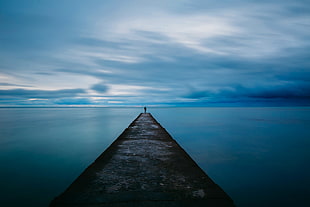 man standing on dock beside body of water HD wallpaper