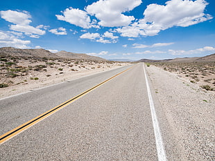 grey asphalt road under blue and white cloudy sky during daytime