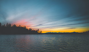 body of water near mountain under orange sunset