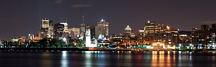 gray concrete buildings turned-on lights near sea during nighttime